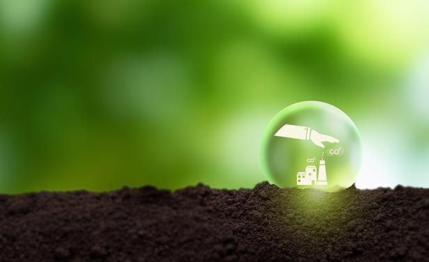 Illustration symbolique de la réduction des émissions de CO₂, avec une main protégeant un site industriel dans une bulle verte posée sur de la terre