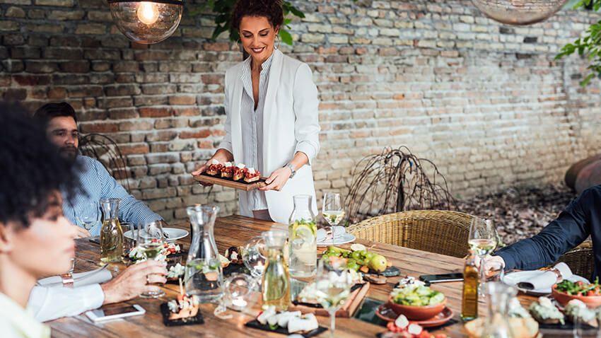 Un femme porte un plateau repas devant une table bien garnie.