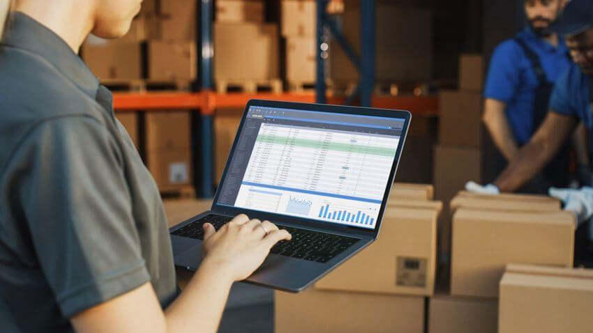 Un homme tape sur le clavier d'un ordinateur portable dans un entrepôt.