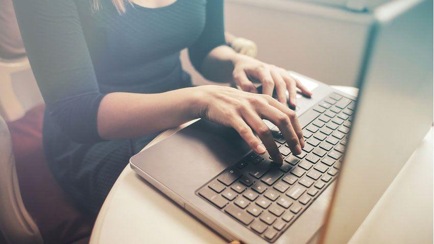 Une femme tape sur le clavier de son ordinateur depuis son domicile.