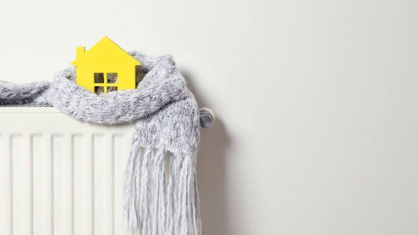 Une écharpe, posée sur un radiateur, enroule une petite maison jaune.