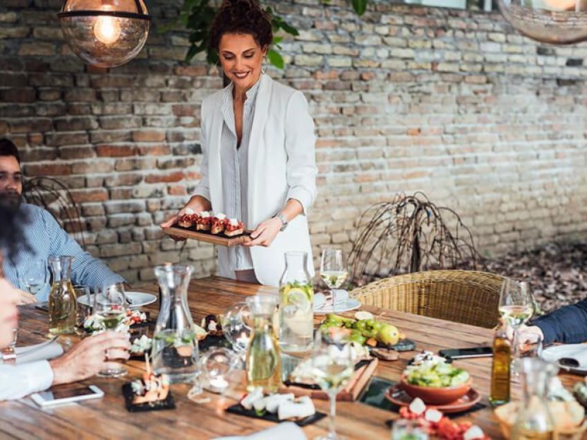 Un femme porte un plateau repas devant une table bien garnie.