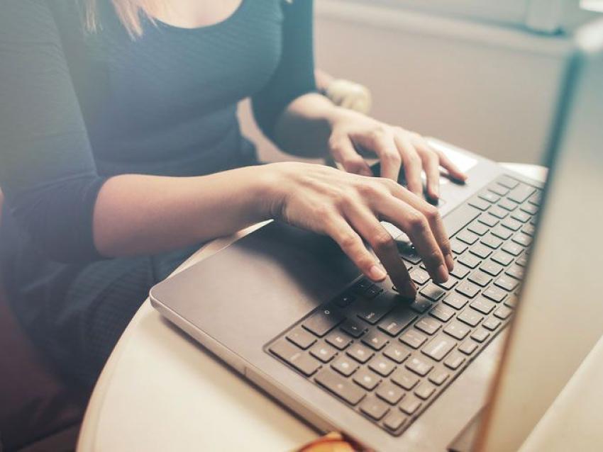 Une femme tape sur le clavier de son ordinateur depuis son domicile.