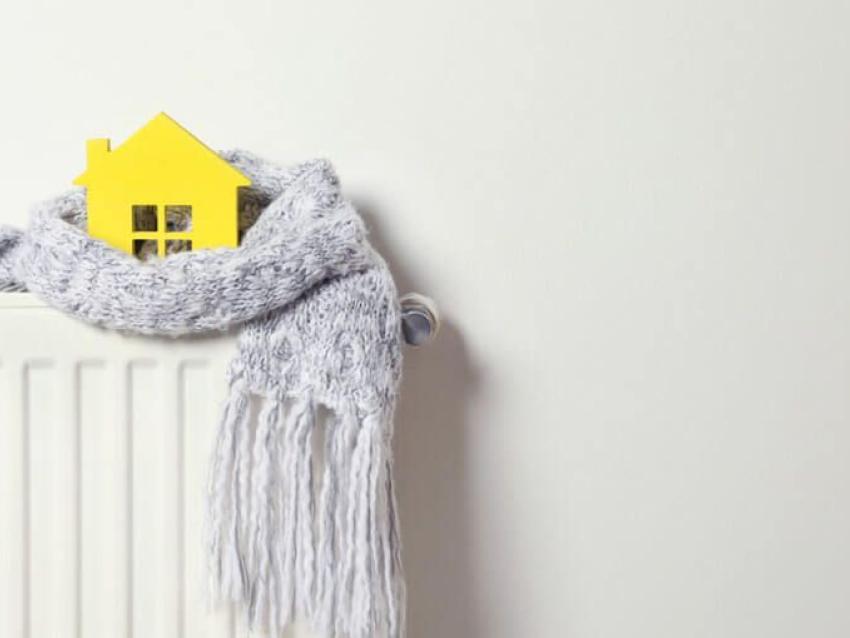 Une écharpe, posée sur un radiateur, enroule une petite maison jaune.